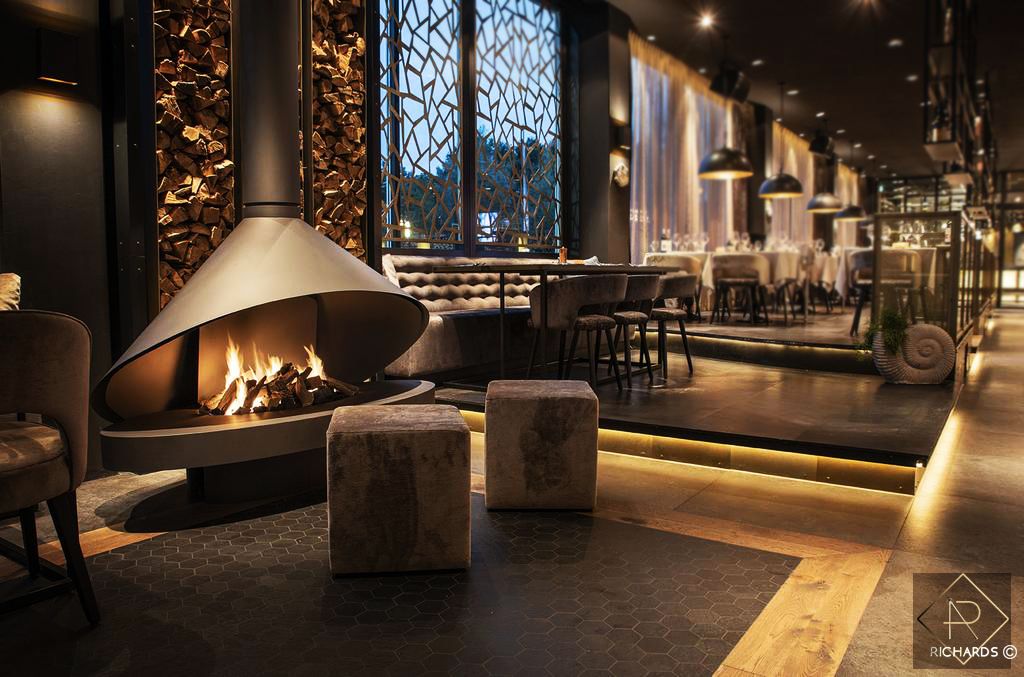 Ammonite lounge concept — fireplace, stacked wood and warm ambient lighting